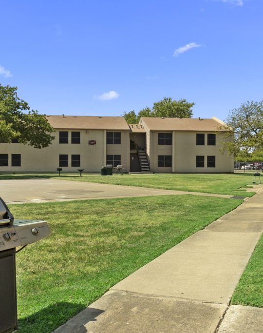 a grill and a lawn area in front of apartment buildings at The Northwood Apartments