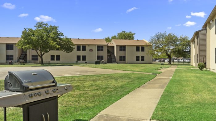 a grill and a lawn area in front of apartment buildings at The Northwood Apartments