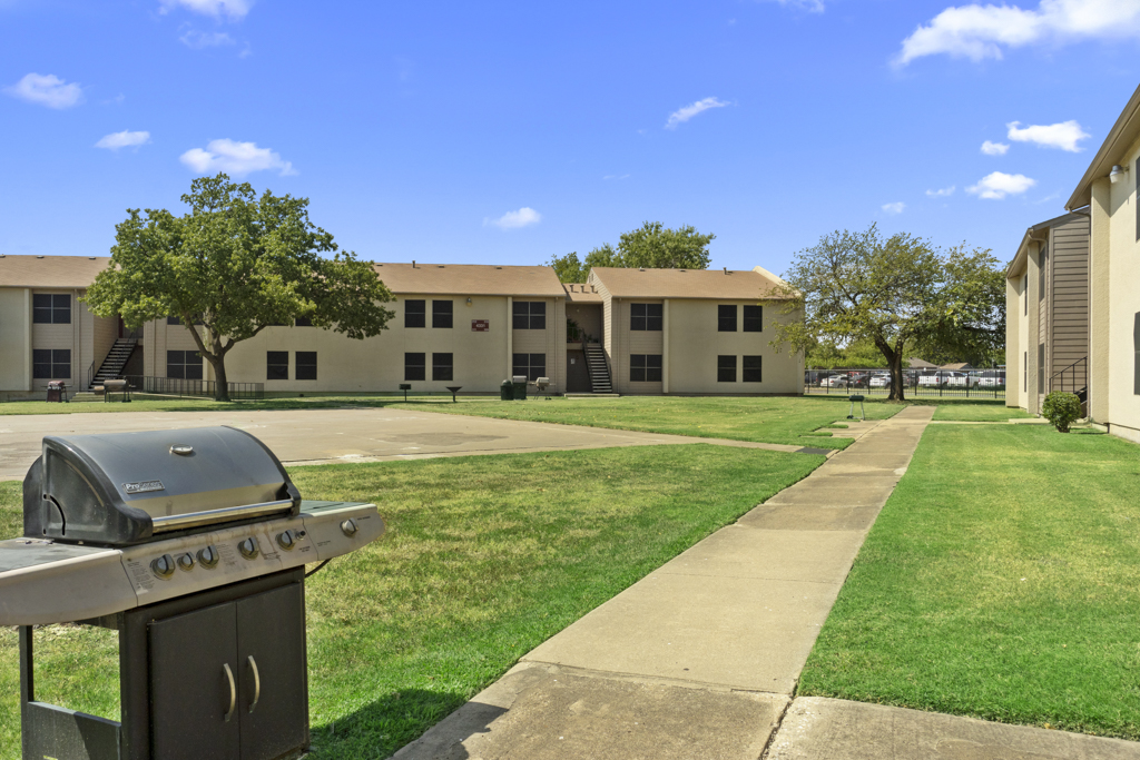 a grill and a lawn area in front of apartment buildings at The Northwood Apartments